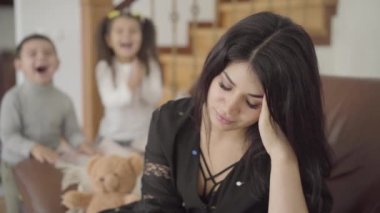 Koltukta oturan yorgun bir Orta Doğulu annenin portresi ve arka planda zıplayan iki küçük çocuğu. Güzel bir kadın elleriyle başını tutuyor ve tatlı kızı yukarı geliyor..