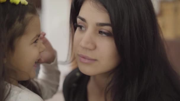 Närbild porträtt av en söt Mellanöstern flicka med lockigt hår viskar i hennes mödrar öra. En vacker kvinna med hasselögon som skvallrar med sin dotter. Lycklig familj vilar hemma. — Stockvideo