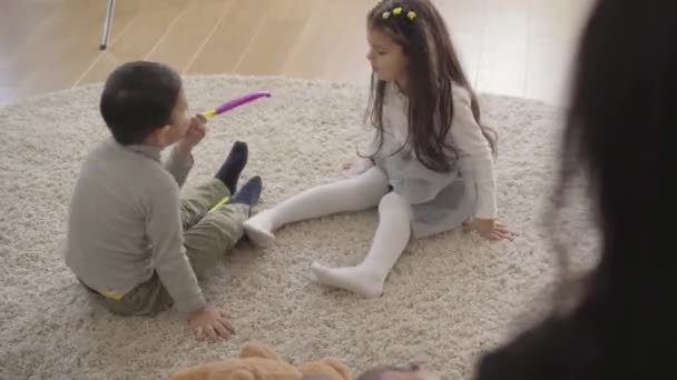 Dos lindos niños de Oriente Medio jugando con silbatos de fiesta en la alfombra suave en casa. Amistosos hermanos pasar tiempo libre juntos en el interior . — Vídeos de Stock