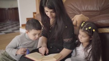 Büyüleyici Orta Doğulu kadın küçük çocuklara kitap okuyor. Anne, sevgili oğlunu ve kızını evde eğitiyor..