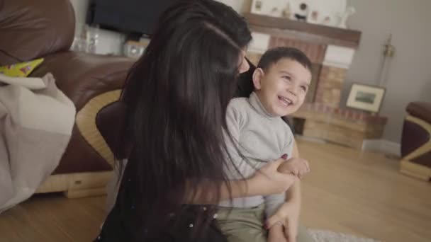 Retrato de un juguetón chico de Middle Eatern imitando el vuelo en avión. Alegre madre con el pelo largo y oscuro jugando con un niño sonriente en casa. Cámara moviéndose dinámicamente siguiendo a las personas . — Vídeos de Stock