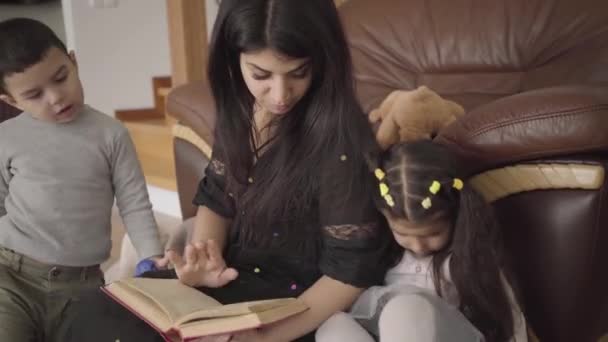 Csinos közel-keleti nő, aki kisgyerekeknek olvassa a könyvet. Anya otthon neveli kedves fiát és lányát.. — Stock videók