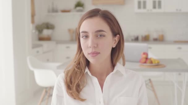 Retrato de una joven niña caucásica sonriente sentada en la cocina moderna y luminosa. Mujer bonita pasar los fines de semana en casa . — Vídeo de stock