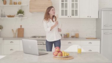 Gündelik giysiler içinde, modern mutfakta tahta kaşıklarla dans eden mutlu beyaz kız. Mutlu güzel kadın hafta sonlarını evde geçiriyor..