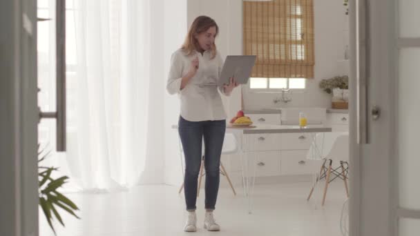 Menina muito caucasiana recebendo boas notícias do laptop e pulando. Jovem alegre comunicando on-line a partir de casa . — Vídeo de Stock