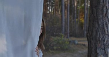 Beyaz giysilerden bakıp gülümseyen güzel beyaz bir kadın. Çekici pozitif kız ormanda sakin bir yaz gününün tadını çıkarıyor..