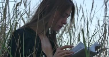 Güzel beyaz esmer kız çimlerin üzerinde oturmuş kitap okuyor. Güzel kadın gölün kıyısında sessizliğin tadını çıkarıyor..