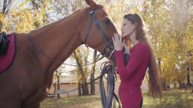 Beyaz atlı, uzun kıvırcık saçlı, at gözlerine bakıp gülümseyen çekici bir kadın binici. Pembe elbiseli esmer beyaz bir kızın güzel evcil hayvanıyla dışarıda dinlendiği portresi..