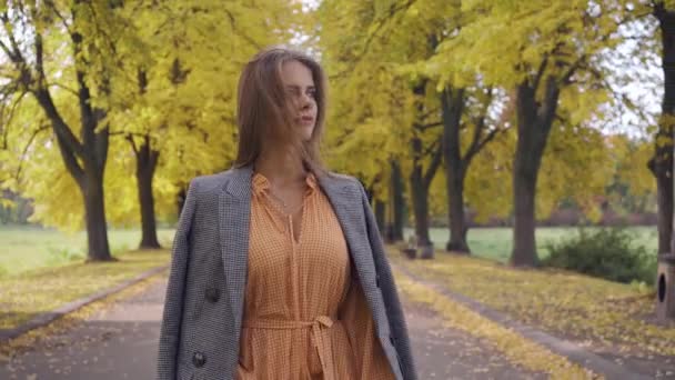 Retrato de una chica morena sonriente con vestido de mostaza y chaqueta a cuadros caminando por la carretera. Niza mujer caucásica paseando en el parque de otoño los fines de semana . — Vídeos de Stock