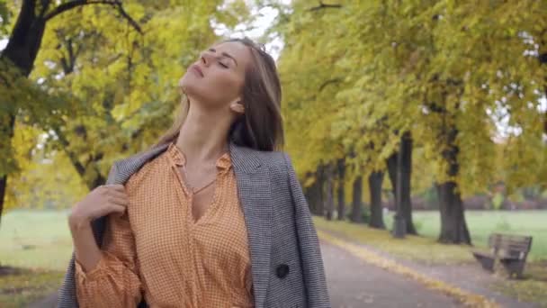 Primer plano de una chica caucásica confiada en vestido de mostaza y chaqueta a cuadros caminando por el camino. Mujer morena bonita paseando en el parque de otoño los fines de semana . — Vídeos de Stock