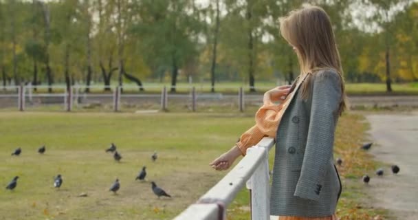 Seitenansicht einer attraktiven kaukasischen Frau mit langen braunen Haaren, die neben dem Gehege im Herbstpark steht. hübsches Mädchen in karierter Jacke, das sich im Freien ausruht. Kino 4k Filmmaterial prores hq. — Stockvideo
