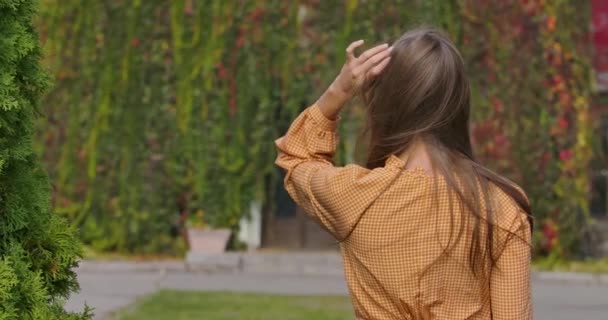 Visszapillantás egy fiatal fehér lányra mustáros ruhában, lúdtalppal. Elegáns nő fogdossa a hosszú barna haját. Mozi 4k felvételek Prores Hq. — Stock videók