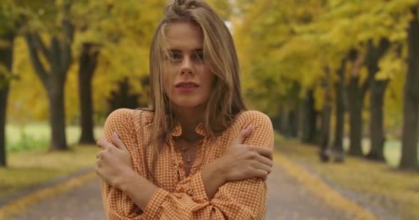Freezed Caucasian girl with brown hair and pleasant smile standing on the road in the autumn park. Pretty woman in mustard dress with crows feet print posing at camera. Cinema 4k footage ProRes HQ. — ストック動画