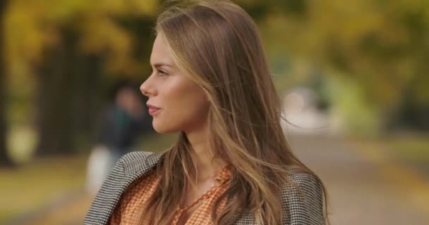 Perfil retrato de la hermosa mujer caucásica de pie en el parque de otoño y sonriendo. Chica encantadora en chaqueta a cuadros y vestido de mostaza girando a la cámara y metiendo el pelo. Cinema 4k metraje ProRes HQ . — Vídeos de Stock