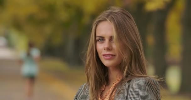 Close-up of beautiful Caucasian woman standing in autumn park and smiling to camera. Attractive mysterious girl in checkered jacket and mustard dress posing outdoors. Cinema 4k footage ProRes HQ. — ストック動画