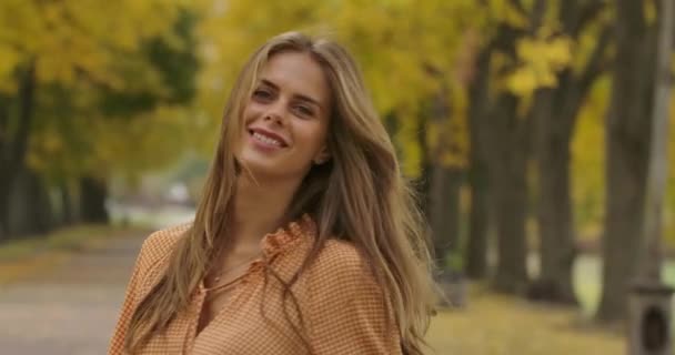 Smiling Caucasian woman with long brown hair and green eyes spinning in the autumn park. Elegant girl in mustard dress with crows feet print having fun in the autumn park. Cinema 4k footage ProRes HQ — ストック動画