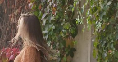 Genç esmer, beyaz bir kız kameraya gülümsüyor. Karga ayaklı hardal elbiseli olumlu bir kadın sonbahar parkında boş zaman geçiriyor. Sinema 4k görüntüleri Prores Hq.