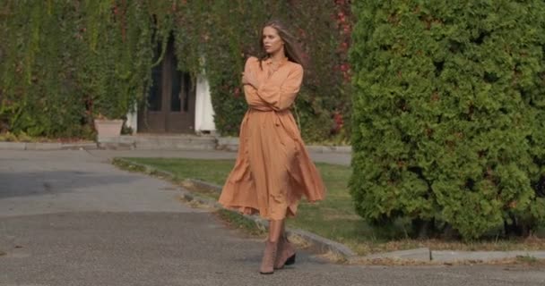 Hermosa chica caucásica en vestido de mostaza disfrutando del día de otoño al aire libre. Encantadora chica de pelo castaño largo que pasa su tiempo libre al aire libre. Cinema 4k metraje ProRes HQ . — Vídeo de stock