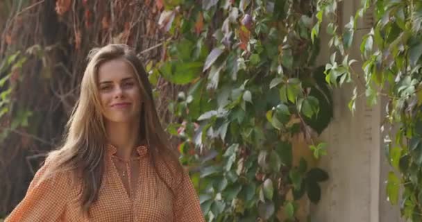 Joven morena caucásica girando y sonriendo a la cámara. Mujer positiva en vestido de mostaza con patas de gallo estampado pasar tiempo libre en el parque de otoño. Cinema 4k metraje ProRes HQ . — Vídeos de Stock