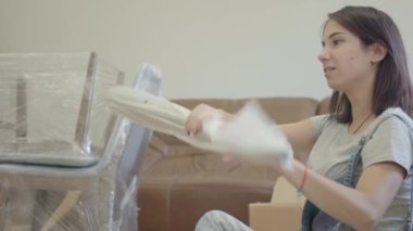 Oturma odasında paketleri açan gülümseyen beyaz bir kadın. Yeni evi döşeyen güzel bir kız. Bayan aydınlık, modern daireye taşınıyor..