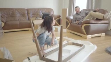 Oturma odasında, arka planda yatan kocası ya da erkek arkadaşı olarak toplanan beyaz bir kadının portresi. Pozitif aile yeni evi döşüyor. İçeri giriyoruz..