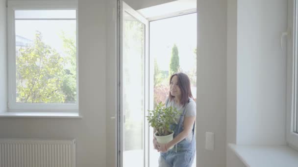 Young excited Caucasian couple coming into their new house holding box and home plant. Happy family moving in a big light house. Start of new life. — Stockvideo