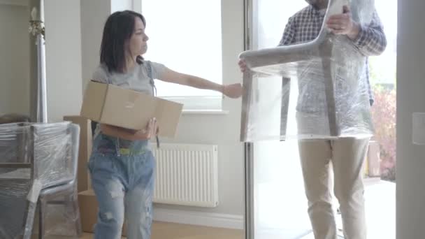 Família caucasiana jovem trazendo móveis novos na casa que eles acabaram de comprar. Um casal feliz a mudar-se para cá. Início de uma nova vida . — Vídeo de Stock