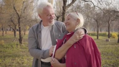 Mutlu Kafkasyalı emekli çiftin yakın plan portresi. Sonbahar ormanlarında güneş ışığında durup sarılıyorlar. Olgun Avrupalı bir aile güneşli bir akşamı dışarıda geçiriyor. Birlikte yaşlanmak, sonsuz aşk kavramı.