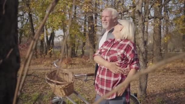 Porträtt av lyckliga vita pensionerade par som står i solljus i höstskogen eller parken och kramas. Gammal europeisk familj spenderar solig kväll utomhus. Åldrande tillsammans, evig kärlek koncept. — Stockvideo