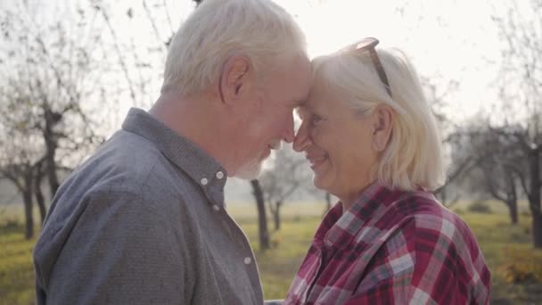 Portret van een glimlachende oudere blanke familie die in het zonlicht staat met gebogen hoofden. Gelukkig volwassen Europees echtpaar brengt zonnige avond buiten door. Samen ouder worden, eeuwig liefdesconcept. — Stockvideo