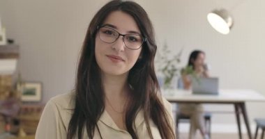 Gözlüklü genç beyaz kız kameraya bakıyor ve gülümsüyor. Arkadaşı ya da kız kardeşi masada arka planda oturuyor. Evde dinlenen pozitif kadınlar. Sinema 4k görüntüleri Prores Hq.