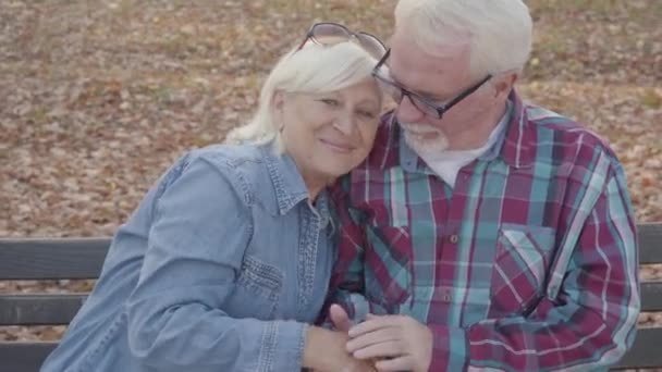 Starší evropský pár sedí na lavičce a mluví. Starší manžel uklidňuje svou krásnou starší ženu. Stárnoucí, věčný koncept lásky. — Stock video