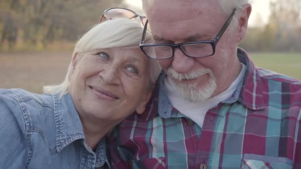 Facce di primo piano di famiglia caucasica più anziana seduta in parco di autunno e sorridente. Maturo coppia europea trascorrere serate assolate all'aria aperta. Invecchiare insieme, eterno concetto di amore . — Video Stock