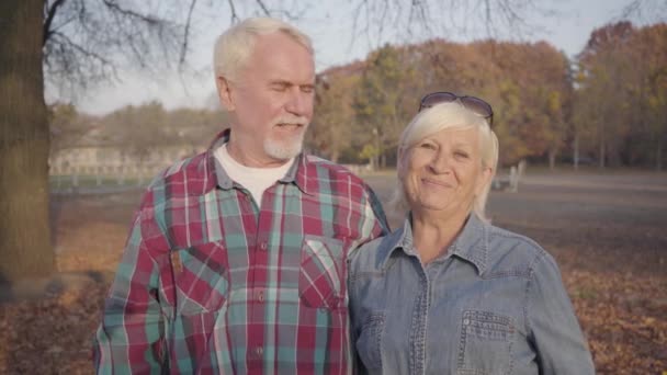 Ancianos Caucásico marido y mujer de pie en la luz del sol en el parque de otoño y hablando a cámara. Pareja europea madura pasando tiempo juntos al aire libre. Envejecer juntos, concepto de amor eterno . — Vídeo de stock