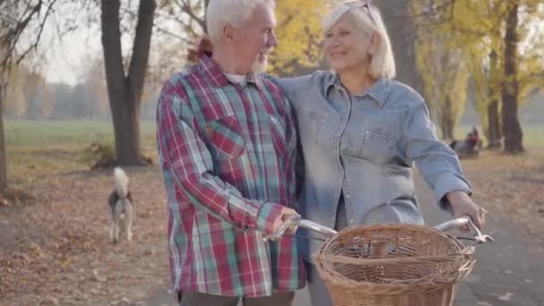 Feliz padre de familia caucásica de pie en el parque de otoño con bicicleta y hablando. Sonriendo pareja madura jubilada pasando la noche de otoño al aire libre. Envejecer juntos, concepto de amor eterno . — Vídeo de stock