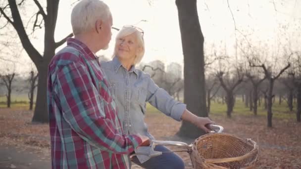 Feliz mujer caucásica mayor de pie en el parque de otoño y mirando a su adorable marido. Pareja jubilada madura pasando la noche de otoño al aire libre. Envejecer juntos, concepto de amor eterno . — Vídeos de Stock