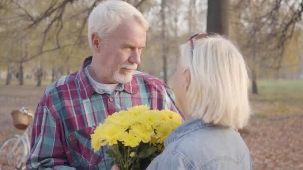 成熟した白人男性は菊の花束で彼の愛らしい妻を見て、彼女と話をします.肯定的なヨーロッパの成熟した家族は秋の公園でロマンチックな夜を過ごす。一緒に高齢化、永遠の愛 — ストック動画