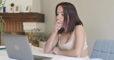 Laptopta yazı yazan düşünceli beyaz kadının portresi masada oturuyordu. Evde online çalışan güzel bir kız. Sinema 4k görüntüleri Prores Hq.