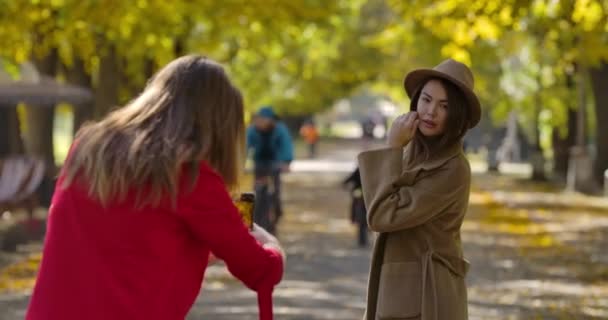 아름다운 코카서스 소녀는 가을 공원 주변에서 사진을 찍고 있는 여자 친구를 위해 포즈를 취하고 있습니다. 젊은 유럽 여성들 이 야외에서 사진 촬영을 하고 있습니다. 영화 4K 필름 프로 레스 HQ — 비디오