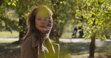 Sonbahar parkında sarı yaprakların arkasında duran güzel beyaz bir kızın portresi. Güzel Avrupalı kadın kameraya bakıyor ve gülümsüyor. Sinema 4k görüntüleri Prores Hq.