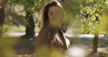 Güz parkında sarı yaprakların arkasında duran tüylü saç kesimi ve hoş gülüşü olan güzel beyaz bir kız. Dışarıda kameraya poz veren güzel Avrupalı bir kadın. Sinema 4k görüntüleri Prores Hq.