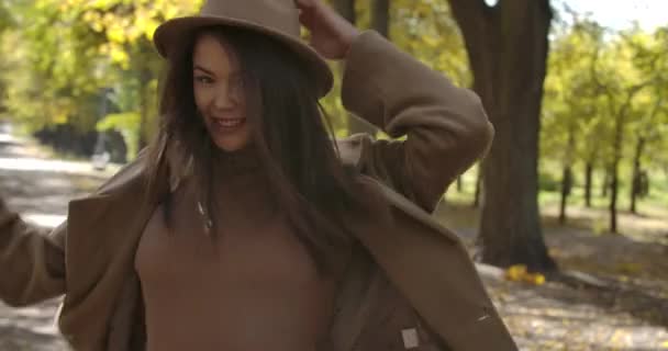 Menina branca sorridente em chapéu elegante girando no parque de outono. Mulher europeia encantadora com sorriso agradável e cabelo castanho se divertindo ao ar livre. Cinema 4k footage ProRes HQ . — Vídeo de Stock