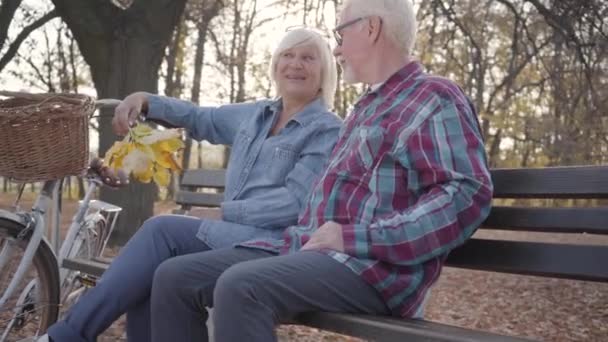 Feliz casal maduro caucasiano sentado no banco à luz do sol e falando. Família europeia sênior passando a noite ensolarada ao ar livre. Envelhecimento juntos, conceito de amor eterno . — Vídeo de Stock