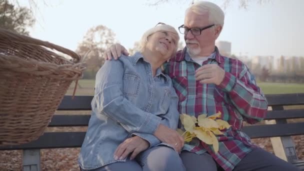 Famille retraitée caucasienne souriante assise sur le banc au soleil et parlant. Couple européen mature passant une soirée ensoleillée en plein air. Vieillir ensemble, concept d'amour éternel . — Video