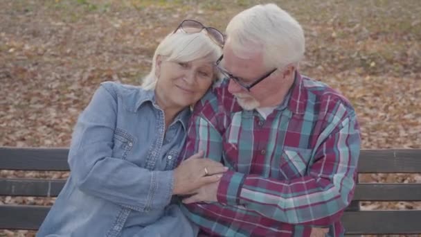 ベンチに座って話している白人のシニアカップルの肖像画。成熟した夫は彼の美しいシニア妻を落ち着かせる。一緒に高齢化、永遠の愛の概念. — ストック動画