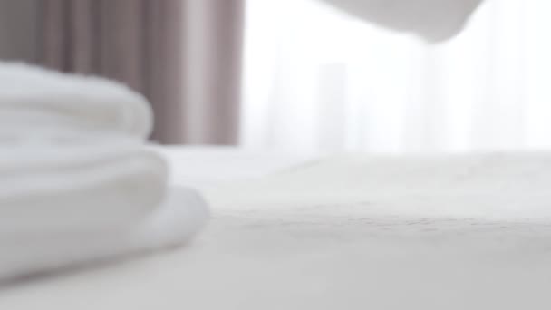Zbliżenie żeńskich białych rąk kładących białe ręczniki na łóżku i prostujących je. Nierozpoznawalna pokojówka przygotowująca sypialnię w ośrodku w słoneczny dzień. Praca, służba, styl życia. — Wideo stockowe