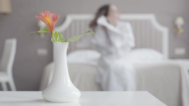 Wazige vrouw veegt nat haar met handdoek in de hotelkamer. Vaas met bloem op de voorgrond. Onherkenbare vrouwelijke toerist rustend na de douche in accommodaties in het resort. Toerisme, vrije tijd. — Stockvideo