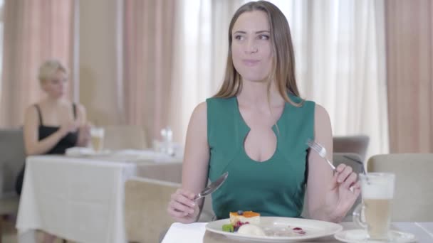 Orgullosa mujer caucásica comiendo cereza dulce con helado en el restaurante. Retrato de chica morena confiada en vestido verde degustación de postre en la cafetería. Alegría, comida dulce, ocio, estilo de vida . — Vídeo de stock