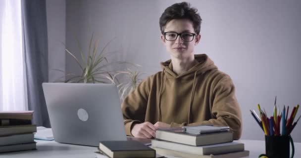 Kluger kaukasischer Junge zeigt Daumen hoch und lächelt in die Kamera. Porträt eines intelligenten männlichen College-Studenten, der zu Hause Hausaufgaben macht. Bildung, Lebensstil, Intelligenz. Cinema 4k ProRes Hauptquartier. — Stockvideo