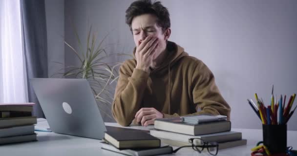 Brunette boy yawning and looking out the window. Portrait of diligent nerd Caucasian college student doing homework. Lifestyle, overworking, education. Cinema 4k ProRes HQ. — Stock Video